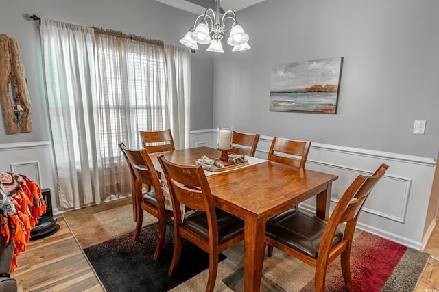 dining area with light wood finished floors, a chandelier, a decorative wall, and wainscoting