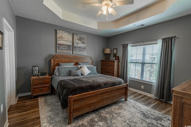 bedroom with a textured ceiling, wood finished floors, a raised ceiling, and baseboards