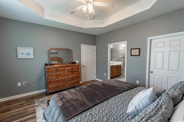 bedroom featuring a raised ceiling, ceiling fan, a textured ceiling, wood finished floors, and baseboards