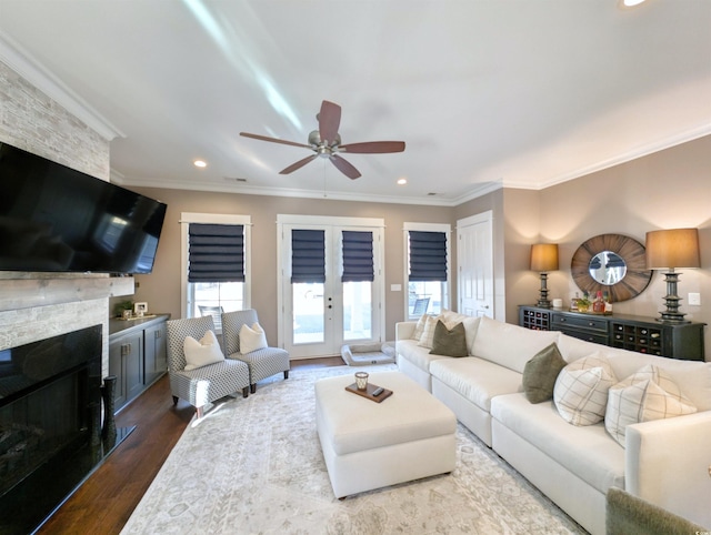 living room featuring a ceiling fan, ornamental molding, wood finished floors, a stone fireplace, and recessed lighting