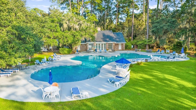 community pool featuring a patio area, a lawn, and an outbuilding