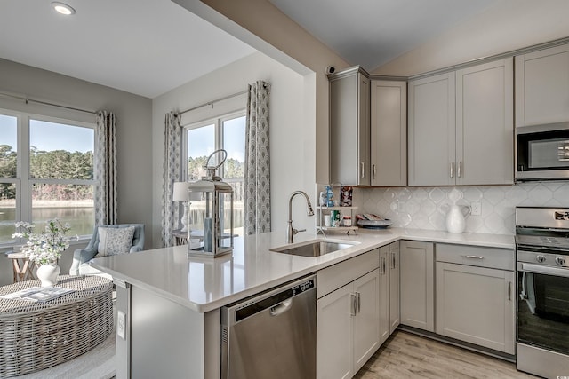 kitchen with light countertops, gray cabinets, tasteful backsplash, a sink, and stainless steel appliances