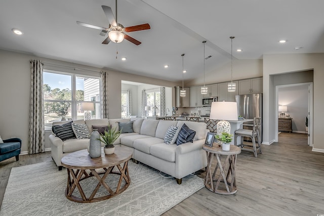 living area with a ceiling fan, baseboards, vaulted ceiling, and light wood-style floors