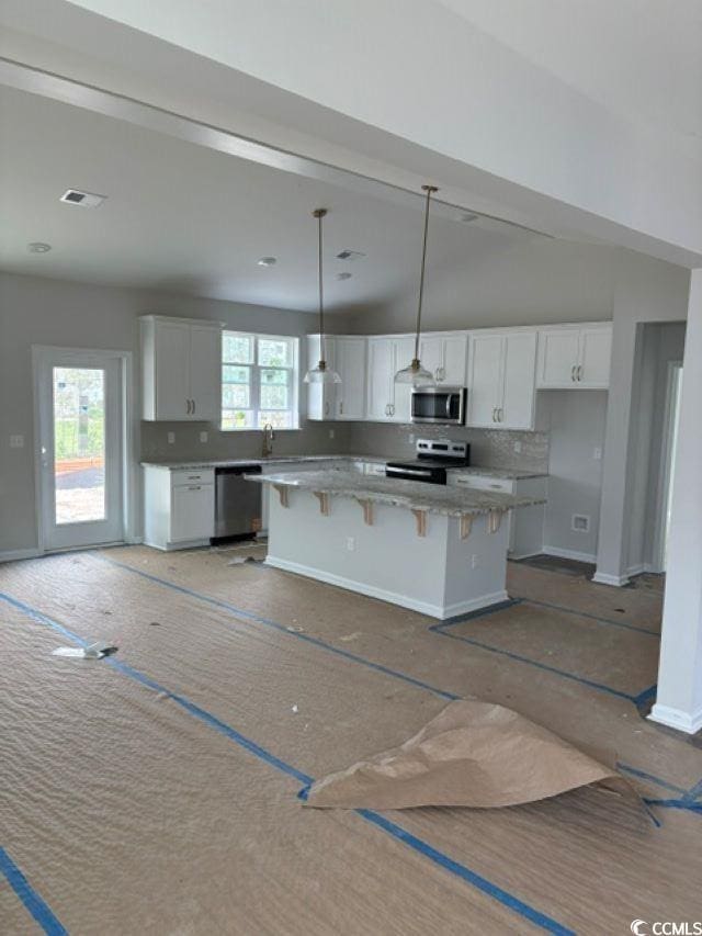 kitchen with stainless steel appliances, white cabinetry, a kitchen island, and a breakfast bar area