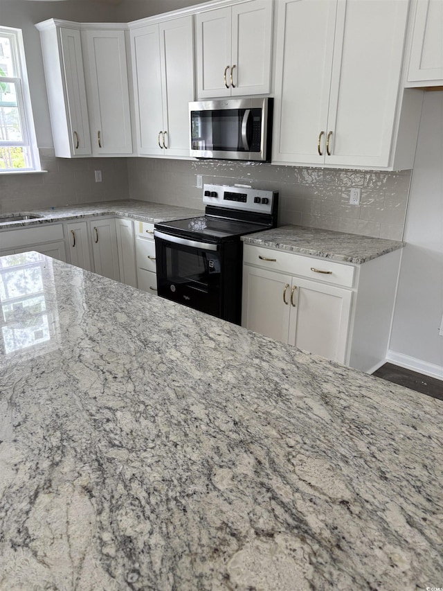 kitchen with stainless steel microwave, black range with electric stovetop, white cabinetry, and light stone countertops