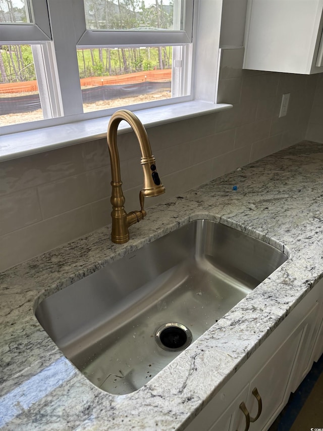 interior details with a sink, backsplash, white cabinets, and light stone countertops
