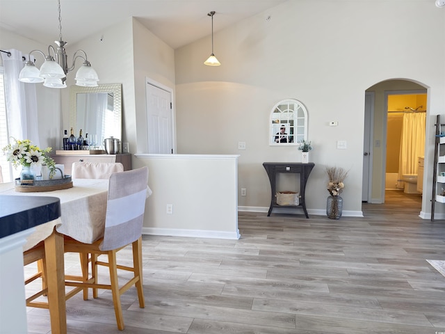 dining space featuring arched walkways, high vaulted ceiling, a notable chandelier, a healthy amount of sunlight, and light wood-type flooring