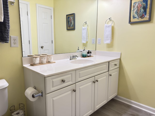 half bath featuring toilet, baseboards, wood finished floors, and vanity