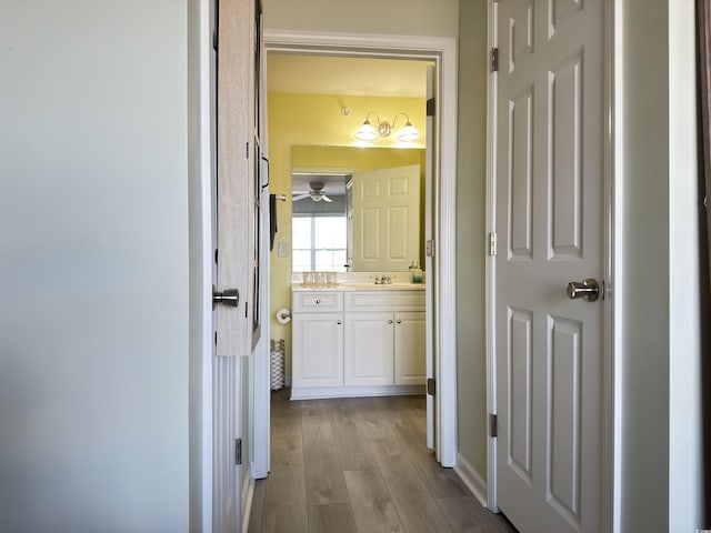 corridor with light wood finished floors and a sink