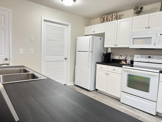 kitchen with white appliances, a sink, white cabinetry, light wood finished floors, and dark countertops