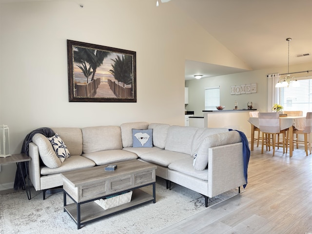 living area with visible vents, vaulted ceiling, a notable chandelier, and light wood finished floors