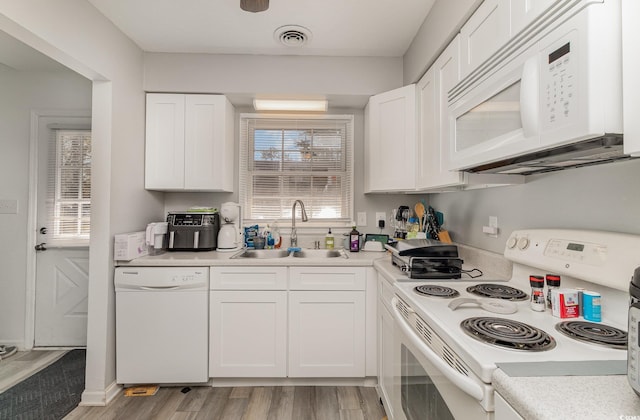 kitchen featuring visible vents, light wood-style floors, white cabinets, a sink, and white appliances