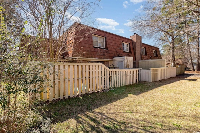 exterior space featuring mansard roof, a chimney, fence, a yard, and brick siding