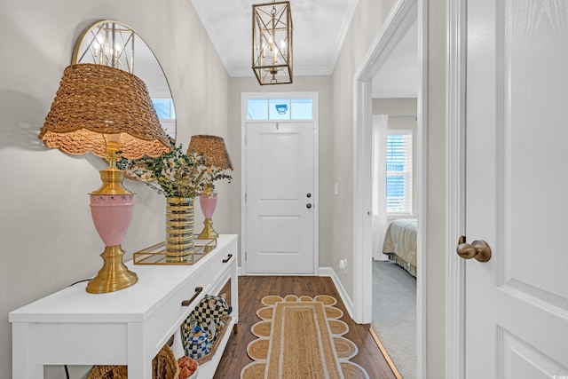 entryway with ornamental molding, dark wood-type flooring, baseboards, and an inviting chandelier