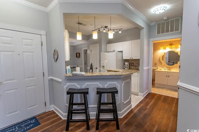 kitchen with white refrigerator with ice dispenser, a breakfast bar, visible vents, white cabinetry, and dark wood finished floors