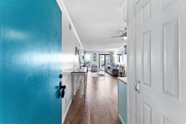 hall featuring a textured ceiling, ornamental molding, dark wood-style flooring, and visible vents