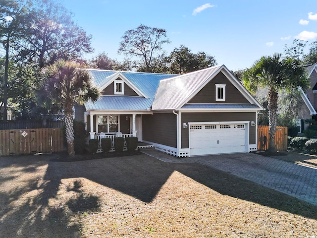 view of front facade with covered porch, metal roof, decorative driveway, and fence