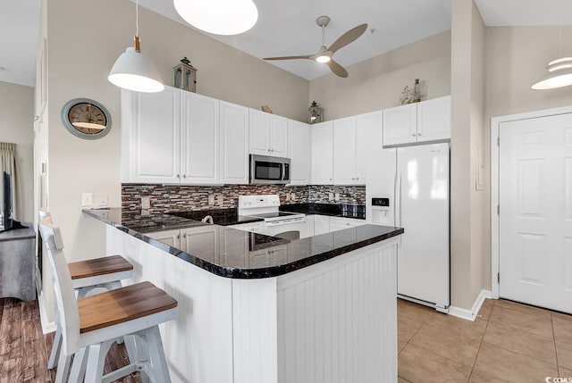 kitchen featuring a peninsula, white appliances, a kitchen bar, and hanging light fixtures