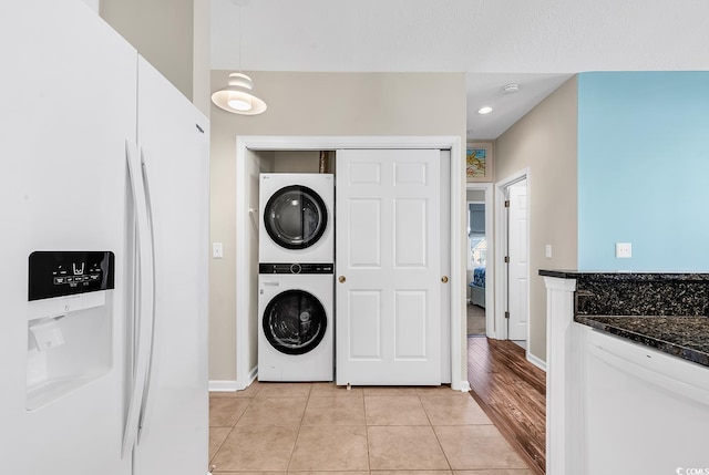 washroom featuring light tile patterned floors, laundry area, baseboards, and stacked washer / drying machine