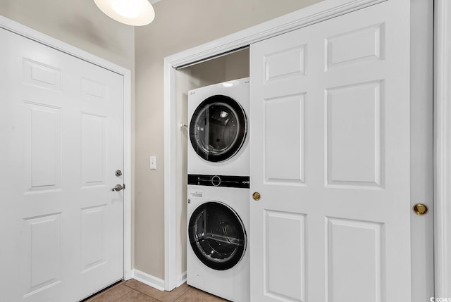 washroom featuring stacked washing maching and dryer, baseboards, light tile patterned floors, and laundry area