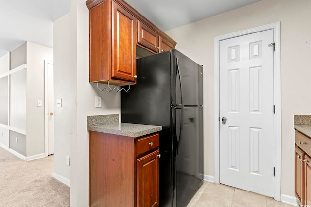 kitchen with brown cabinets, light tile patterned floors, light countertops, freestanding refrigerator, and baseboards