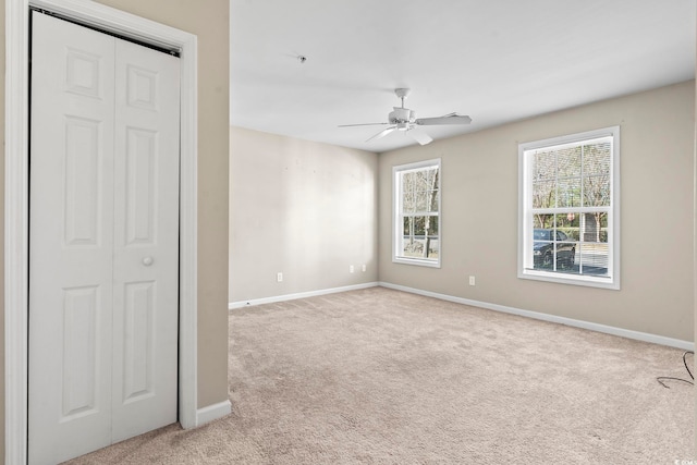 unfurnished bedroom with light carpet, ceiling fan, a closet, and baseboards