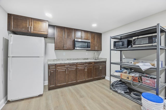 kitchen with light wood finished floors, stainless steel microwave, freestanding refrigerator, a sink, and black microwave