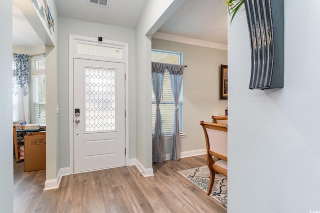 foyer featuring light wood finished floors, baseboards, visible vents, and crown molding