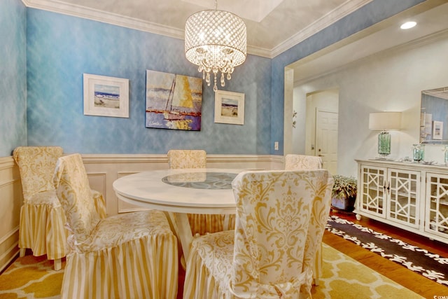 dining area with a wainscoted wall, crown molding, a notable chandelier, a decorative wall, and wood finished floors