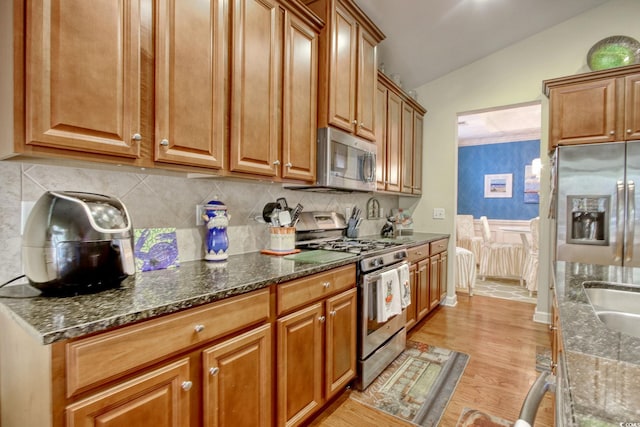 kitchen featuring brown cabinets, stainless steel appliances, dark stone countertops, and lofted ceiling