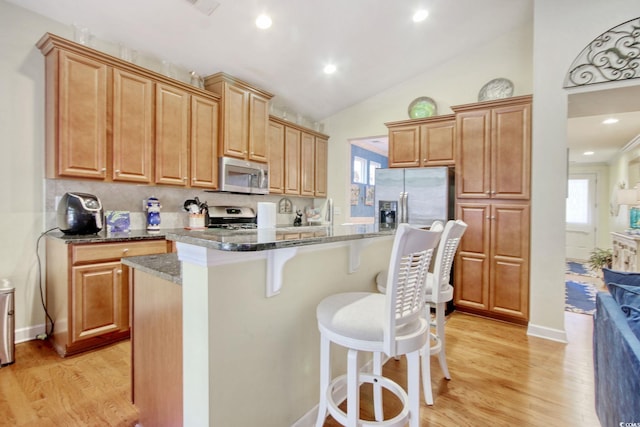 kitchen featuring plenty of natural light, a center island with sink, dark stone counters, appliances with stainless steel finishes, and a kitchen bar