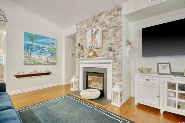 unfurnished living room with a glass covered fireplace, vaulted ceiling, baseboards, and wood finished floors