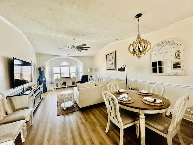 dining space with a textured ceiling, arched walkways, wood finished floors, vaulted ceiling, and crown molding