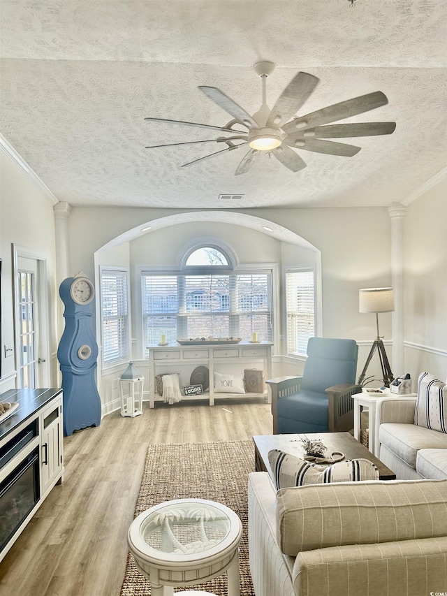 living area featuring visible vents, ceiling fan, ornamental molding, wood finished floors, and a textured ceiling