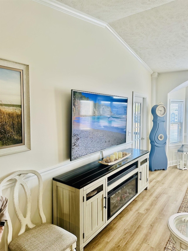 interior space with lofted ceiling, a textured ceiling, arched walkways, light wood-style flooring, and crown molding