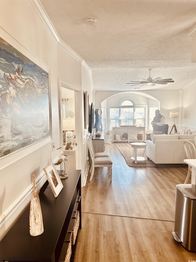 living room featuring arched walkways, ceiling fan, ornamental molding, wood finished floors, and a textured ceiling