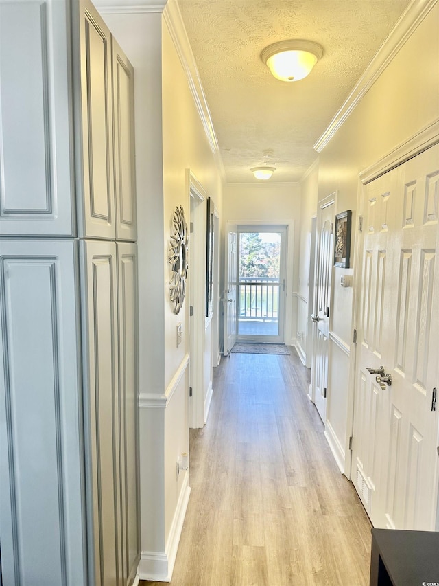 hall with light wood finished floors, ornamental molding, a textured ceiling, and visible vents