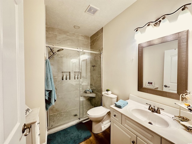 full bath with a textured ceiling, toilet, vanity, visible vents, and a shower stall