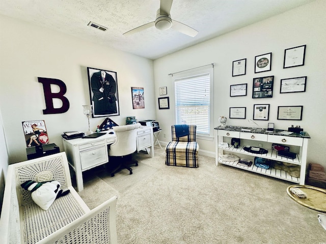 office featuring a textured ceiling, light colored carpet, a ceiling fan, baseboards, and visible vents