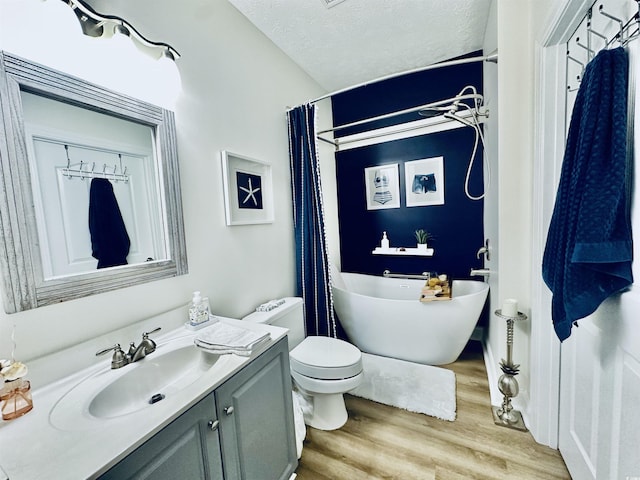 bathroom featuring a textured ceiling, toilet, wood finished floors, vanity, and a freestanding bath