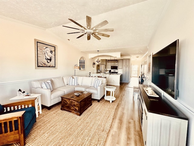 living area with a ceiling fan, lofted ceiling, a textured ceiling, and light wood finished floors