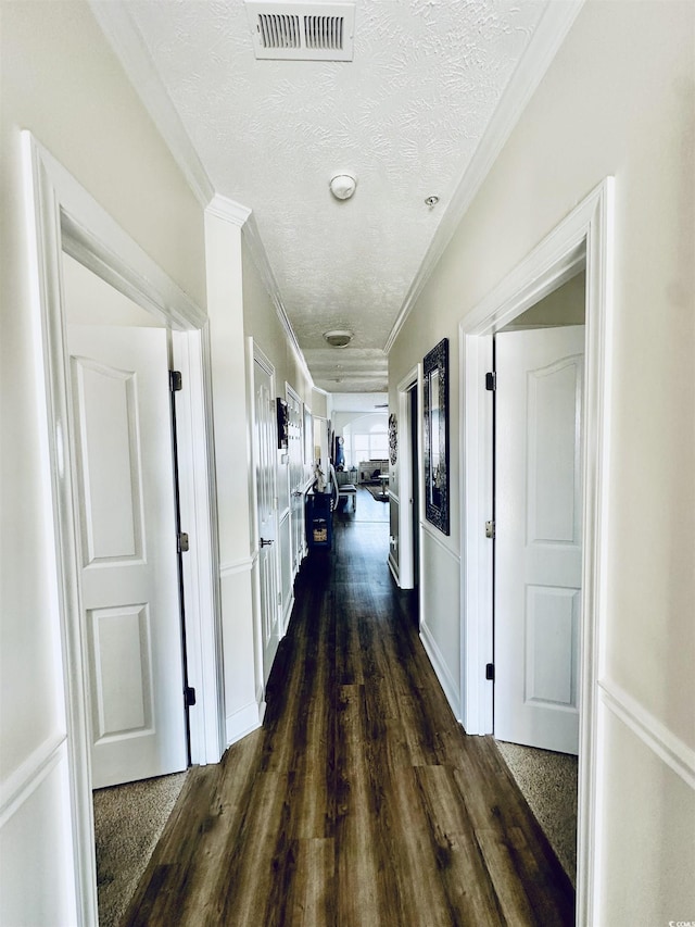 corridor with a textured ceiling, dark wood-style flooring, visible vents, and crown molding