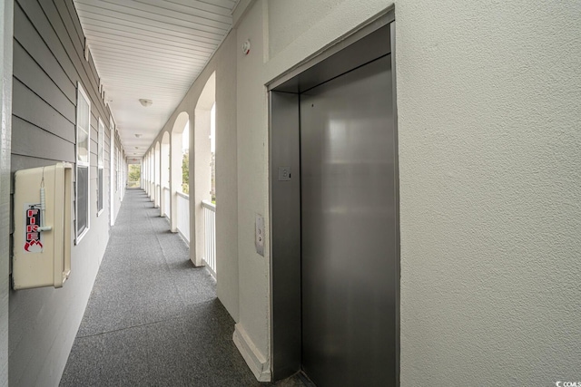 hallway featuring a textured wall, dark carpet, and elevator