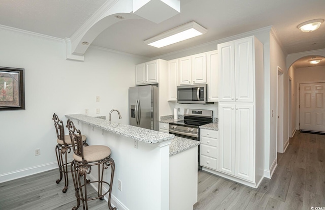 kitchen featuring arched walkways, a breakfast bar, stainless steel appliances, white cabinetry, and a peninsula