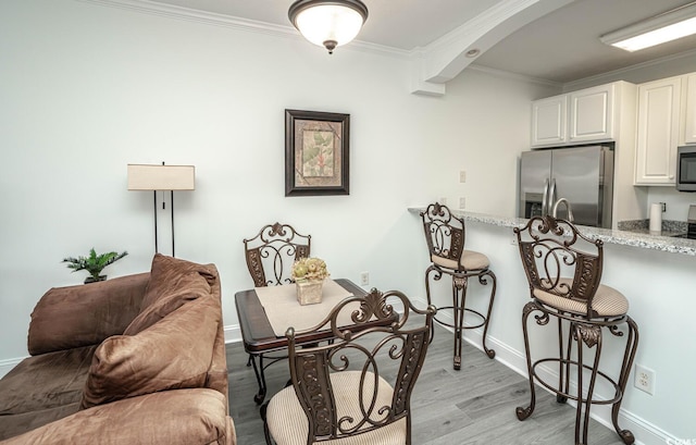 dining space featuring arched walkways, ornamental molding, light wood finished floors, and baseboards