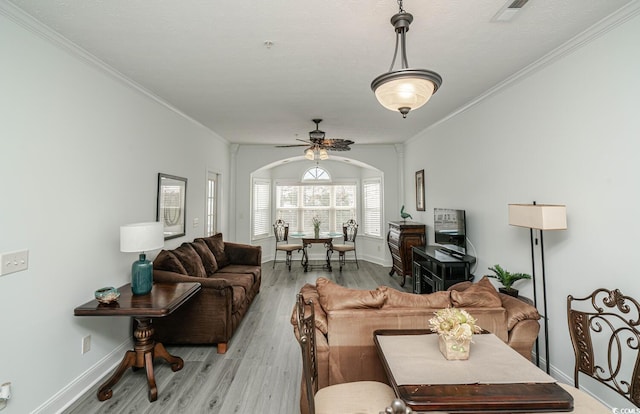 living area with light wood-style floors, arched walkways, visible vents, and crown molding