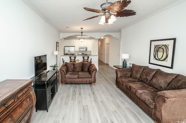 living room featuring arched walkways, a ceiling fan, a textured ceiling, crown molding, and light wood-type flooring