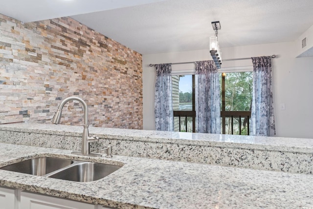 kitchen with a textured ceiling, light stone counters, a sink, white cabinets, and pendant lighting