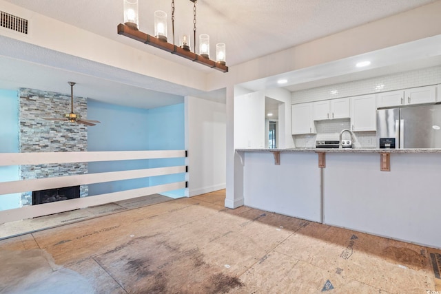 kitchen with visible vents, white cabinets, decorative backsplash, stainless steel fridge, and pendant lighting