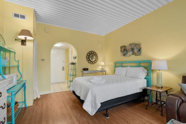 bedroom featuring light wood-style floors, visible vents, and arched walkways